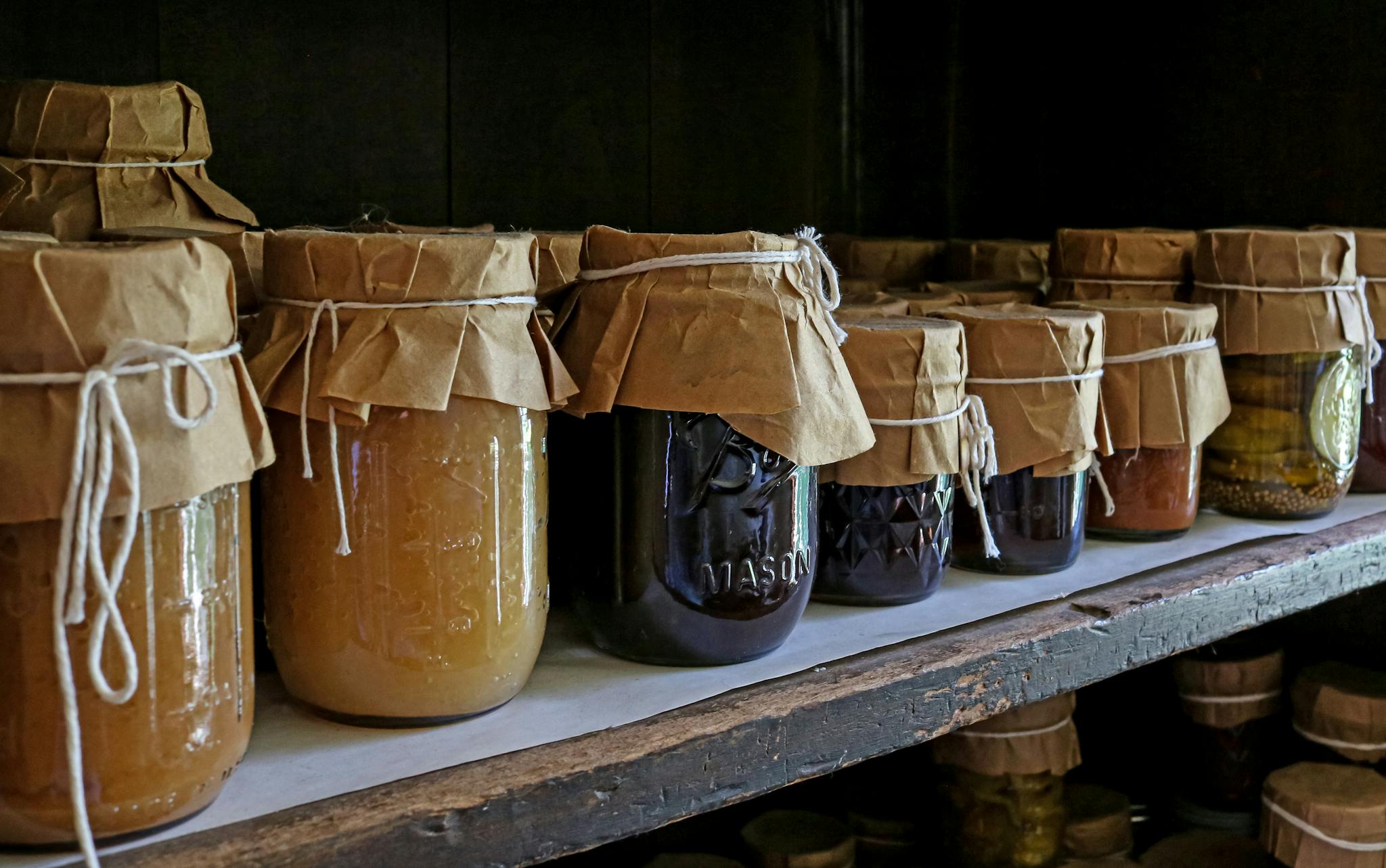 Assorted preserved foods in glass jars on a wooden shelf, showcasing traditional storage methods.